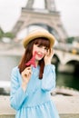 Pretty young girl with red lipstick wearing straw hat and blue dress, holds red lollipop, smiles to camera, standing Royalty Free Stock Photo