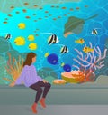 The pretty young girl sits near the big aquarium and looks at the colorful underwater world Royalty Free Stock Photo