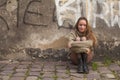 Pretty young girl sitting on the pavement near a stone wall of a house. Walk in the city. Royalty Free Stock Photo