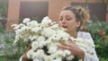 Pretty young girl is standing near a bush of white chrysanthemums in park during spring time, hypersensitivity, asthma