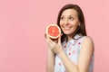 Pretty young girl in summer clothes looking up holding in hand half of fresh ripe grapefruit isolated on pink pastel Royalty Free Stock Photo