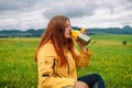 Happy traveler young woman resting in the mountains and drinking tea from thermos at sunset in spring or summer season. Royalty Free Stock Photo