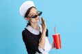 Pretty young girl wearing chambermaid uniform and drinking soda isolated over blue background