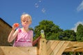 A pretty, young girl wearing a pink dress, blows bubbles from the top of a climbing frame, on a sunny summers day with a deep blue Royalty Free Stock Photo