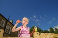 A pretty, young girl wearing a pink dress, blows bubbles from the top of her climbing frame, on a sunny summers day with a deep Royalty Free Stock Photo