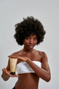 Pretty young half naked african american woman holding body lotion bottle and looking at camera, posing isolated over