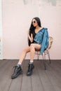 Pretty young hipster woman with long hair in stylish denim clothes in sunglasses in leather autumn boots sits on a vintage chair Royalty Free Stock Photo