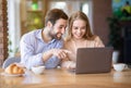 Pretty young lady and her boyfriend browsing web or watching movie on laptop at coffee shop, panorama Royalty Free Stock Photo