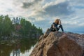 Pretty young lady with red hair sitting on stone near bay shore in summer evening. Tourist on the beautiful landscape background. Royalty Free Stock Photo