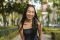 A pretty young lady standing in a park wearing a black strapless tank top and sunglasses, leans forward smiling widely Royalty Free Stock Photo