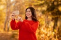 Pretty young lady taking picture of beautiful autumn nature on smartphone camera at park, copy space Royalty Free Stock Photo