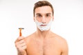 Pretty young man with shaving foam on his cheeks holding a razor Royalty Free Stock Photo