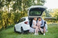 Pretty young married couple and their daughter are resting in the nature. The woman and girl are sitting on open car boot. The man Royalty Free Stock Photo