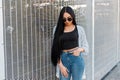 Pretty young modern hipster woman model with long hair in an elegant jacket in round sunglasses in a black T-shirt in jeans Royalty Free Stock Photo