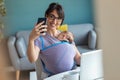 Pretty young mother with her baby in sling taking a selfie while working with laptop at home Royalty Free Stock Photo