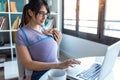 Pretty young mother with her baby in sling working with laptop at home Royalty Free Stock Photo