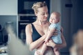 Pretty young mother holding her newborn baby boy standing near kitchen window at home Royalty Free Stock Photo