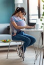 Pretty young mother kissing her baby in sling while working with laptop at home Royalty Free Stock Photo