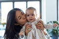 Pretty young mother kissing her little daughter while she looks at the camera at home Royalty Free Stock Photo