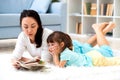 Pretty young mother reading book her little daughter, lying on the carpet on the floor in home Royalty Free Stock Photo