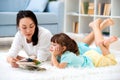 Pretty young mother reading book her little daughter, lying on the carpet on the floor in home Royalty Free Stock Photo