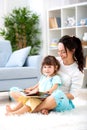 Pretty young mother reading a book to her daughter sitting on the carpet on the floor in the room. Reading with children Royalty Free Stock Photo