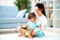 Pretty young mother reading a book to her daughter sitting on the carpet on the floor in the room. Reading with children Royalty Free Stock Photo