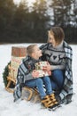 Pretty young mother talk with child son while sitting on the wooden sledge outdoors in winter forest, covered with Royalty Free Stock Photo