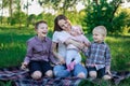 Pretty Young mother with three children sitting on plaid in park. Happy family concept Royalty Free Stock Photo