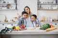 Pretty young mother and two children sons preparing salad with fresh vegetables Royalty Free Stock Photo