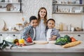 Pretty young mother and two children sons preparing salad with fresh vegetables Royalty Free Stock Photo