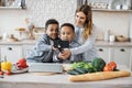 Pretty young mother and two children sons preparing salad with fresh vegetables Royalty Free Stock Photo