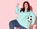 Pretty young overweight woman in jeans, blue hoodie and sunglasses standing with ball holding hand and knee up