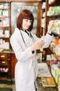 Pretty young pharmacist reading the information about medicine and choosing the product in pharmacy Royalty Free Stock Photo