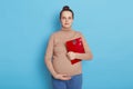 Pretty young pregnant woman holding floor scales in hands, future mother with hair bun touching belly and looking directly at Royalty Free Stock Photo