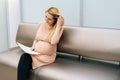 Pretty young pregnant woman is sitting in hallway of hospital waiting to see gynecologist. Royalty Free Stock Photo