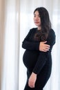 Pretty young pregnant woman standing by the window in room.Concepts of pregnancy and family Royalty Free Stock Photo