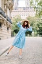 Pretty young red haired lady, wearing elegant blue dress and straw hat, walking in Paris, posing to camera and having Royalty Free Stock Photo