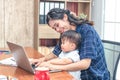 Pretty young single mom working at home on a laptop computer while holding her baby girl sitting on her lap enjoying playing Royalty Free Stock Photo