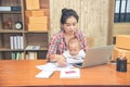 Pretty young single mom working at home on a laptop computer while holding her baby girl sitting on her lap enjoying watching Royalty Free Stock Photo