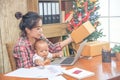 Pretty young single mom working at home on a laptop computer while holding her baby girl sitting on her lap enjoying watching Royalty Free Stock Photo