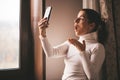 Pretty young smiled Caucasian woman in white turtleneck smiling and videochatting on mobile phone in home.Girl talking Royalty Free Stock Photo