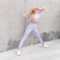 Pretty young sports model woman with sexy slim body in stylish tracksuit doing stretching near the concrete gray wall