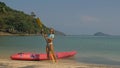 Pretty young sportswoman with sunglasses and swimsuit holds paddle posing near pink plastic canoe on sand beach at Royalty Free Stock Photo