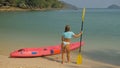 Pretty young sportswoman with sunglasses and swimsuit holds paddle posing near pink plastic canoe on sand beach at Royalty Free Stock Photo