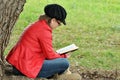 Pretty young teen girl reading book under big tree Royalty Free Stock Photo