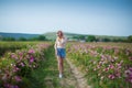 Pretty Young tender woman walking in the tea roses field. Blond lady wearing jeans and retro hat enjoy summer day Royalty Free Stock Photo