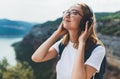 Pretty young tourist woman with backpack and hipster glasses closes her eyes listens favorite music with headphones enjoy