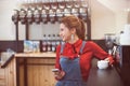 Pretty young trendy woman wearing red shirt and denim casual overalls smiling in coffee house with cellphone in tatoo hand Royalty Free Stock Photo