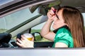 Pretty young woman applying makeup, speaking on phone and drinking coffee while driving Royalty Free Stock Photo